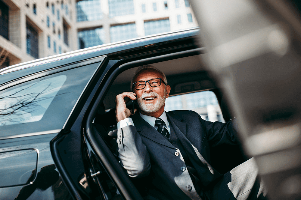 Elderly businessman happily talking on phone in a car.
