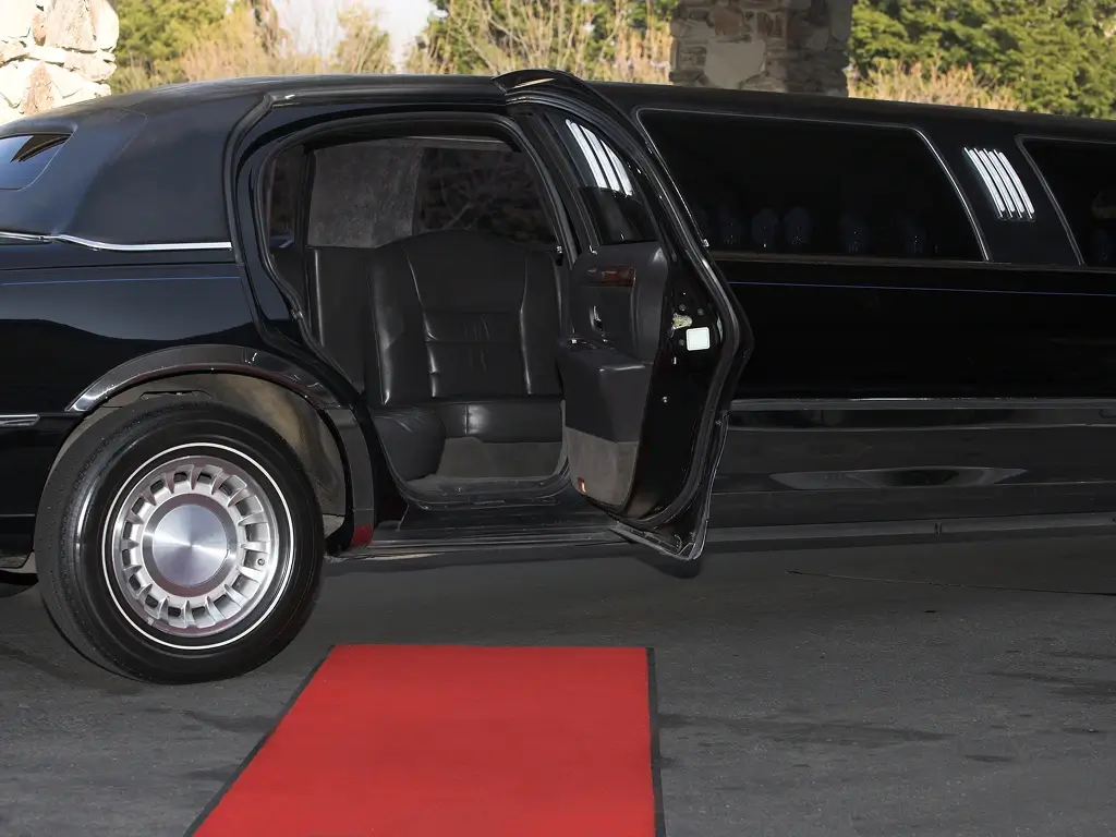 Open limousine door with red carpet on pavement.