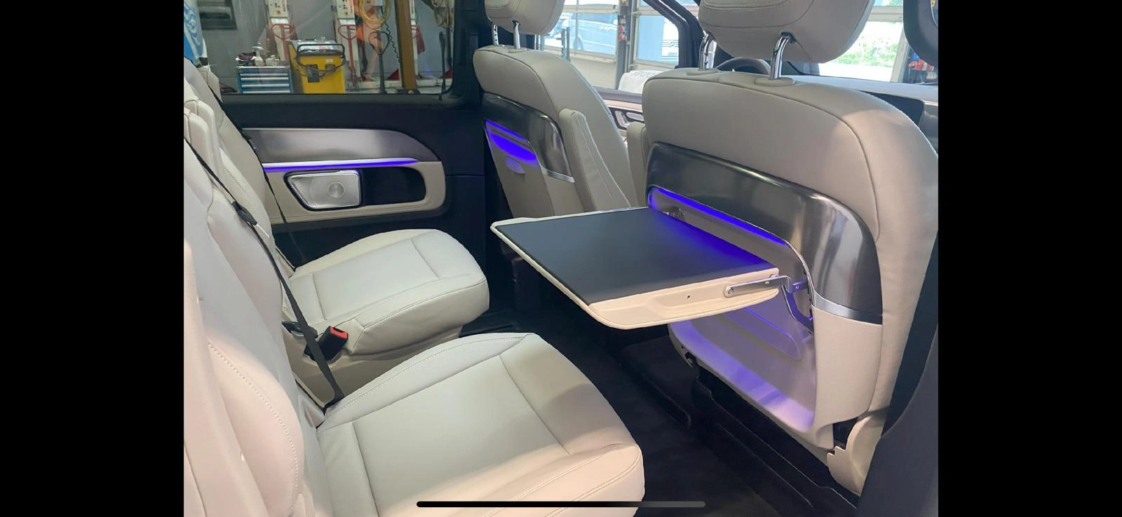 Luxury car interior with illuminated side tray tables and beige leather seats.