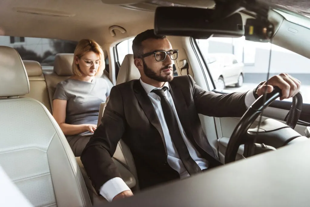 A professional man driving with a woman seated in the back.