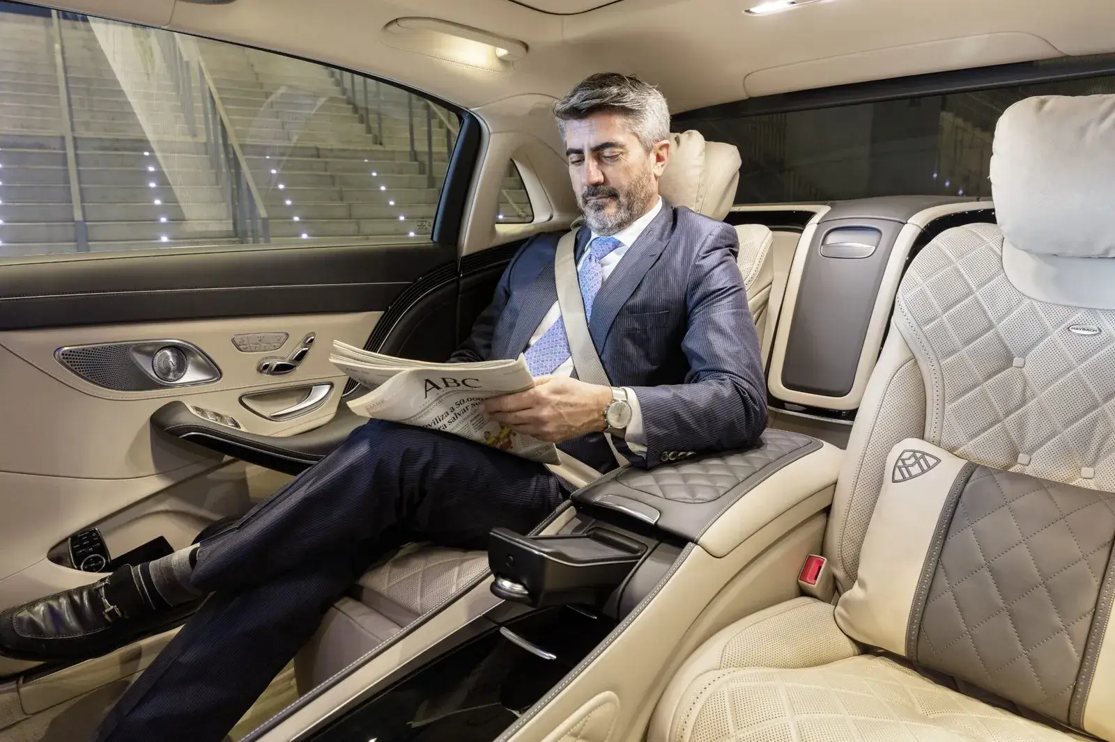 Man in a suit reading a newspaper in a luxury car.