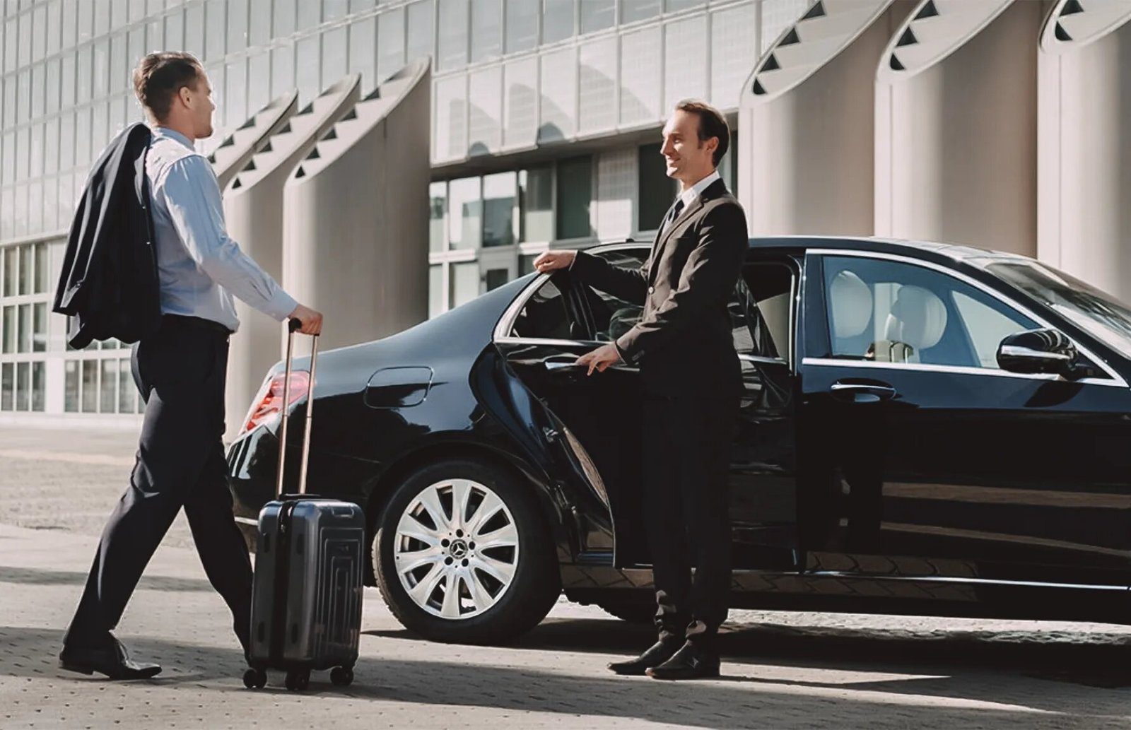 A chauffeur opens the car door for a passenger with luggage.