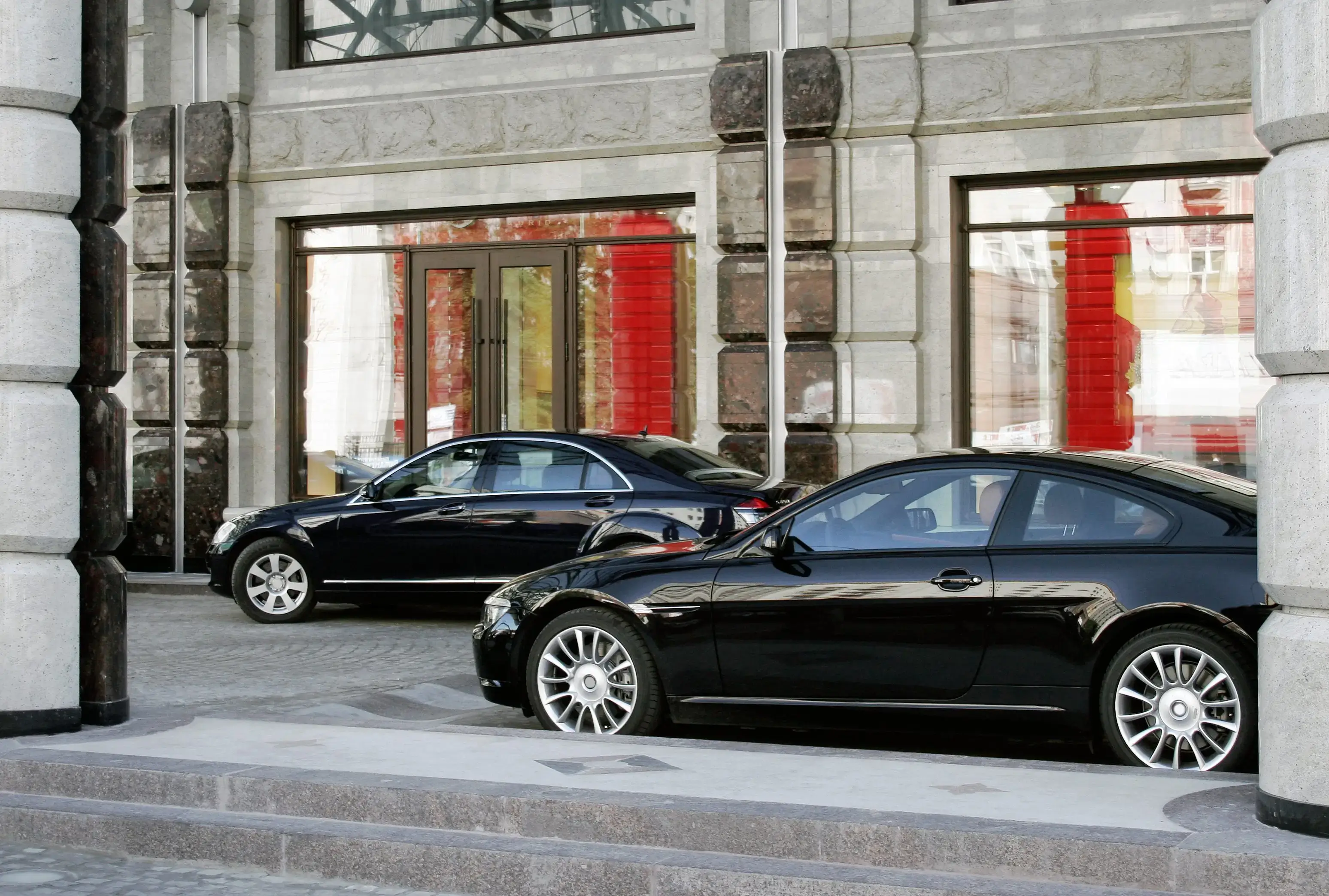 Two sleek black luxury cars parked near a building with large windows.